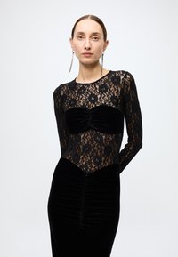 Black lace top with floral pattern and long sleeves. Fitted velvet skirt with ruching, blending textures for contrast and visual interest.