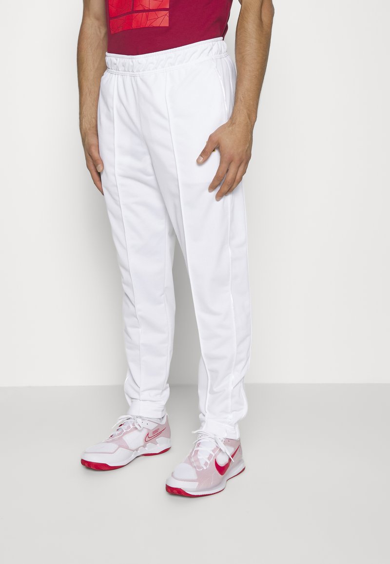 Pantalones deportivos blancos con cintura elástica y franjas laterales. Combinados con zapatillas blancas y rosas, que cuentan con detalles de malla y acentos de logo.