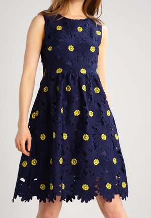 Mørkeblå ærmeløs kjole med stort blomstret blondermønster og gule blomstercentre, skørt med vidde, der ender over knæene.