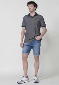 Námořnické polo tričko s texturovaným vzorem, doplněné temným límcem; spárováno se světle modrými denimovými šortkami a bílými teniskami.