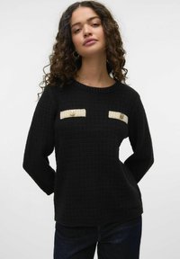 Zwarte sweater met een gestructureerde weving, voorzien van twee witte zakaccenten en gouden knopen. Klassieke ronde halslijn en lange mouwen.