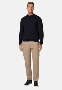 Navy krāsas adīts kreklveida džemperis, kopā ar bēšajiem taisnā piegriezuma biksēm un melnajām tenisa apaviem, ar gludu tekstūru un vienkāršu dizainu.