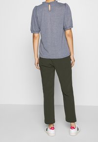 Top gris texturizado con mangas abullonadas y espalda con abertura, combinado con pantalones verde oliva y zapatillas blancas con detalles rojos.