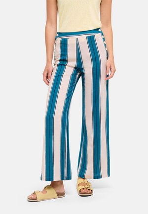 Mujer que lleva pantalones de tiro alto y pierna ancha con rayas verticales en verde azulado y beige y botones laterales, combinados con sandalias amarillas con hebilla.