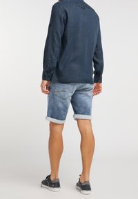 Dżinsowe szorty z jasnym wypraniem, podwiniętymi mankietami, w połączeniu z granatową koszulą na guziki. Koszula ma gładką fakturę i kołnierzyk.