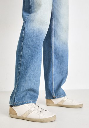 White sneakers with beige accents and textured detailing, paired with light blue, slightly distressed denim jeans, relaxed fit.