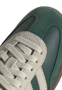 Herrlövålskor med en övre i grönt läder, beige mockadetaljer och vita skosnören. Texturerade detaljer inkluderar zickzack-sömnad och gummisula.