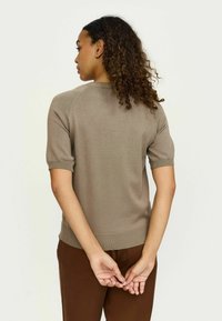 Īsām piedurknēm adīts džemperis maigi brūnā krāsā ar ribotām apkakli un piedurknēm, ar gludu tekstūru un pieguļošu siluetu.