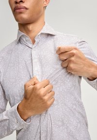 Weißes Hemd mit Paisley-Muster, Knopfkragen und langen Ärmeln, das eine weiche Textur und dezente florale Akzente aufweist.