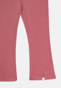 Leggings rose de boca de sino feitos de tecido texturizado. Apresentam costuras nas bainhas e uma pequena etiqueta com o logótipo na parte inferior de uma das pernas.