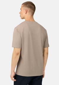 T-shirt a maniche corte in taupe chiaro, con collo rotondo e tessuto morbido. La vista posteriore presenta un design semplice senza decorazioni.
