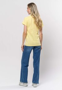 Kollase värvusega lühikeste varrukatega T-särk, mida on kombineeritud plekiliste siniste laiade pükstega. Särgil on sile tekstuur, komplekti kuuluvad ka vabaaja valged tossud.