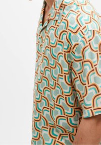 Koszula z krótkim rękawem z retro geometrycznym wzorem w odcieniach teal, brązowym i pomarańczowym na jasnym tle, wykonana z gładkiego, lekkiego materiału.