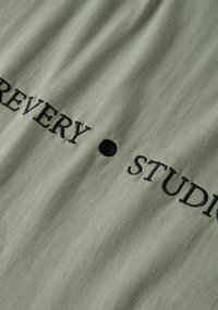 Olive green fabric featuring black embroidered text that reads "RECOVERY • STUDIO." Smooth texture with a subtle sheen.