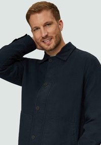 Marineblaue Jacke aus strukturiertem Stoff, mit einem kragenlosen Ausschnitt, Knopfleiste und zwei Fronttaschen.