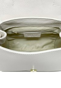 Inuti en vit läderhandväska med mjukt tygfoder, en dragkedjeficka och ett organiseringsfack. Texturerad yta och släta kanter.