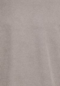 Stickad tröja i en ljus taupe-färg med en vertikal ribbad textur, som har ett mjukt, stretchigt tyg. Inga synliga detaljer eller mönster.