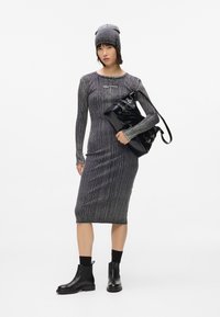 Vestido de punto gris a rayas, de longitud media por debajo de la rodilla, con mangas largas y escote redondo. Bolso de cuero negro y botas negras hasta el tobillo. Gorro gris.
