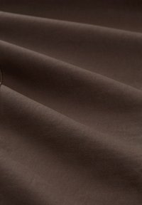 Pogled od blizu na gladak, tamno smeđi materijal s mekim nabiranim dijelovima i suptilnom teksturom, naglašavajući kvalitetu i pada materijala.