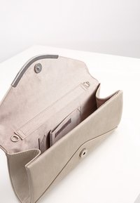 Käsilaukku beigen keinonahan, jossa on taitettava läppä, napin suljettu ja sisätasku järjestelyyn. Sileä pinta ja yksinkertainen muotoilu.