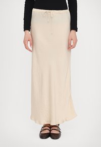 Cream-colored long skirt with a crinkled texture, drawstring waistband, and a flowing shape. Paired with dark flat shoes.