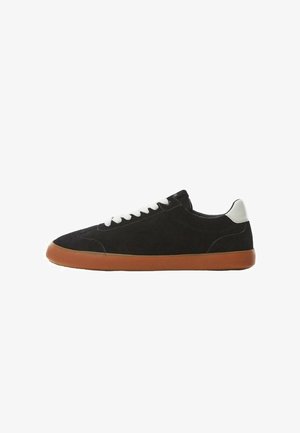 Czarny zamszowy niskoprofilowy sneaker z białymi sznurowadłami, białą taśmą na pięcie i gumową podeszwą, pokazany z profilu na białym tle.