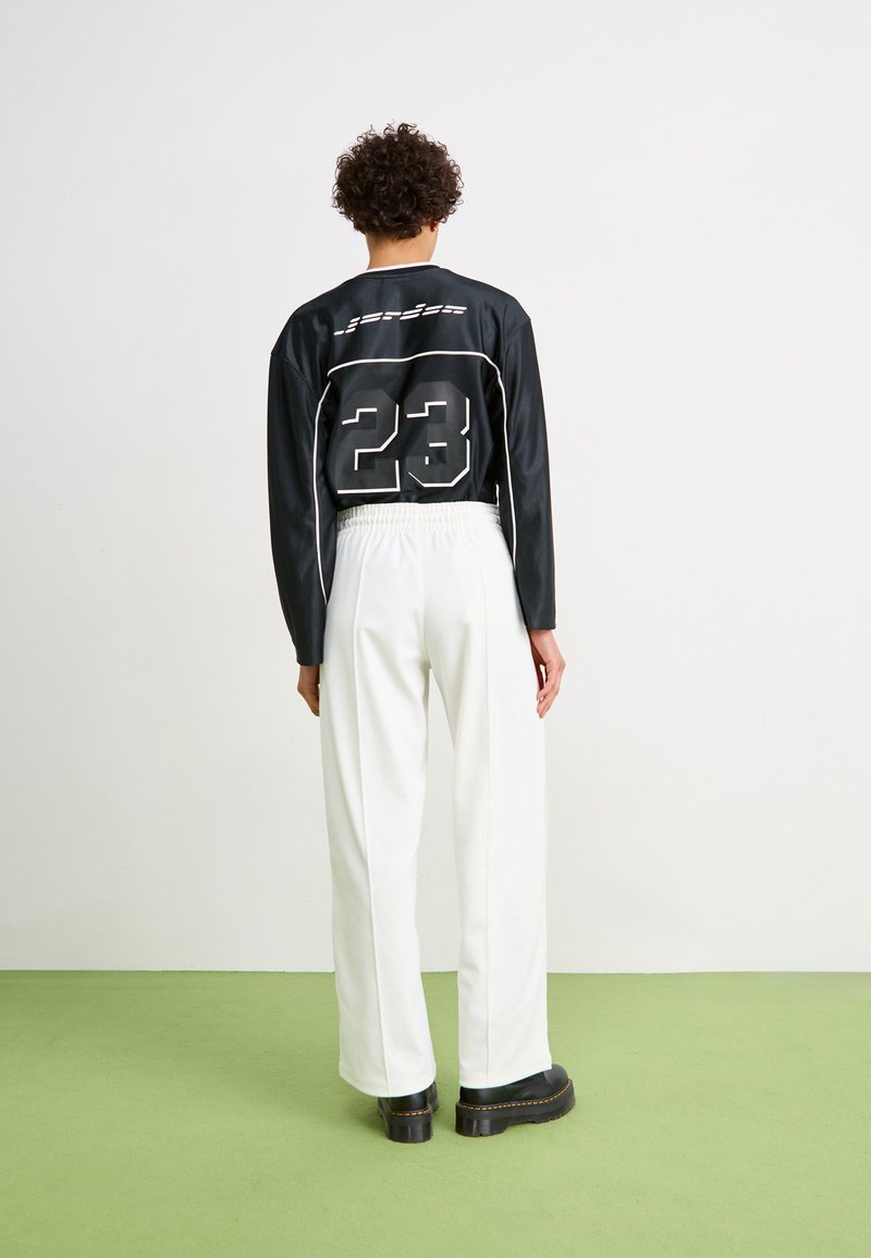 Camisa negra de manga larga con detalles en blanco y el número 23 en la parte de atrás, combinada con pantalones blancos de talle alto y zapatos de plataforma negros.