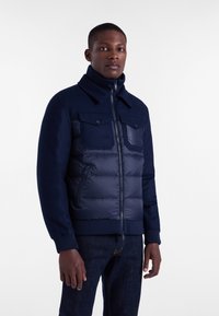 Granatowa kurtka puchowa z wełnianym górnym materiałem, teksturowana tkanina, dwa przednie kieszenie oraz ściągacze przy kołnierzu i mankietach. Zamek błyskawiczny.