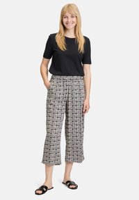 Czarny, krótki top w połączony z spodniami o wysokim stanie, 3/4, z białym wzorem geometrycznym na beżowym tle.