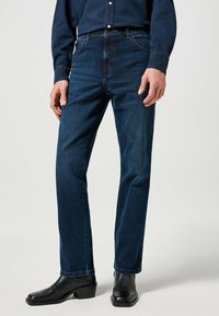 Mörkblå denimjeans med rak passform, med fem fickor och subtila slitningar. Kombinerat med svarta läderstövlar som går till ankeln.