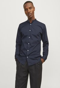 Navig blauwe langekiel met een mandarin-kraag, knoopsluiting en een gladde stof. Draag het met donkergekleurde broeken, het heeft een losse pasvorm.