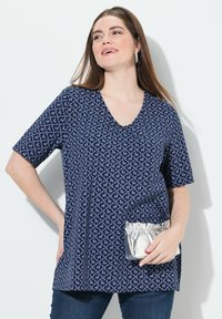 Námořnický modrý top s krátkým rukávem a geometrickým vzorem v světle modré barvě, s výstřihem do V a volným střihem, doplněný stříbrným metalickým psaníčkem.