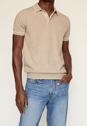 Polo beige à manches courtes avec un tissage texturé, doté d'un col et de poignets contrastants, assorti à un jean bleu clair.