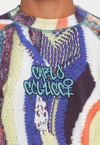 Nærbillede af en flerfarvet tekstureret sweater med blåt broderet graffiti-lignende tekst "CAFILO COLUCCI" på brystet.