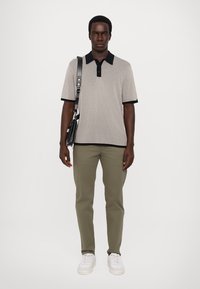 Polo gris à côtes avec un col marine, associé à un pantalon vert olive clair et des baskets blanches. Le mannequin tient un sac à bandoulière noir.