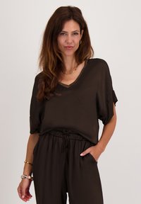 Bruine, kortebloezertop met een brede halslijn en een gestructureerde gouden afwerking. Draagt bijpassende losse broek met een elastische tailleband.