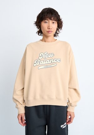 Sweat-shirt beige avec des manches longues et larges et un col rond. Présente le logo "New Balance Athletics" dans une couleur contrastante sur le devant.