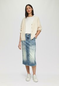 Cremfarbener Strickkarten mit Knöpfen, weißes T-Shirt und verblasener blauer Jeans-Midi-Rock. Weiße Sneaker runden das Outfit ab.
