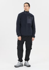 Marine blauwe fleecejack met een gladde voorpaneel, ritszakken, hoge kraag; gecombineerd met zwarte cargo-broeken en grijze wandelschoenen.