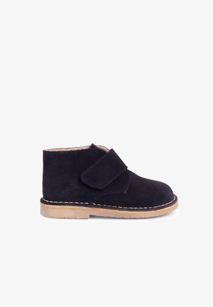 Børns mørkeblå ruskindsstøvle med beige sål og bred velcrolukning på hvid baggrund.