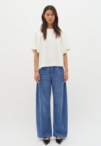 White, lightweight short-sleeve top paired with wide-leg blue denim jeans. Textured fabric, relaxed fit, and raw hems on the jeans.