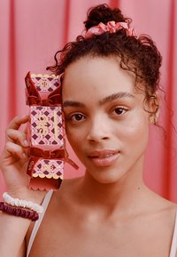 Geschenkset aus drei pinken und roten Boxen mit geometrischem Muster, gebunden mit roten Bändern und mit Branding. Glatte Textur und polierte Oberfläche.