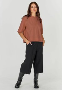 Un top scurt de culoare ruginie, cu un design pătrățos, asociat cu pantaloni negri cu picioare largi și cizme negre până la genunchi. Îmbrăcăminte simplă, modernă.