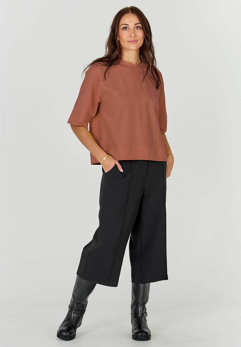 Un top scurt de culoare ruginie, cu un design pătrățos, asociat cu pantaloni negri cu picioare largi și cizme negre până la genunchi. Îmbrăcăminte simplă, modernă.