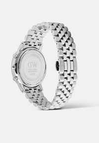 Orologio da polso in acciaio inossidabile argentato con bracciale a maglie, parte posteriore visibile che mostra il nome del marchio, il numero di serie e i dettagli di resistenza all'acqua.