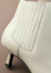 Bottine en cuir blanc avec un design côtelé sur le côté, talon effilé et détail de couture contrasté le long des coutures.