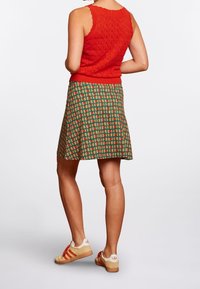 Röd stickad linne med mönstrad grön kjol som har orange och gula mönster, kombinerat med krämfärgade och orange-randiga sneakers.