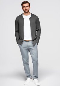 Grå zip-up cardigan over en hvid t-shirt, parret med lysegrå bukser og hvide sneakers. Casual pasform, glat stof og neutrale farver.