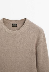 Pull beige en maille avec col ras du cou côtelé, présenté à plat sur un fond blanc.
