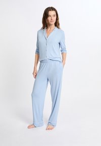 Conjunto de pijama azul claro de manga larga con botones en el frente, ribete blanco en contraste, pantalones de ajuste relajado, hecho de tela suave.